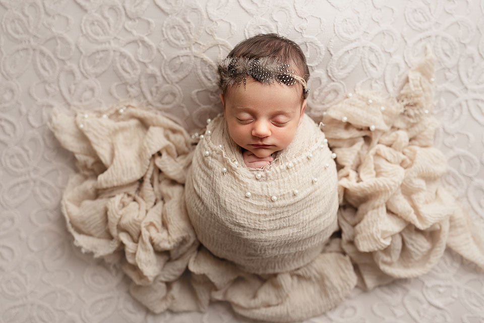 neonata fasciata in crema su wrap damascato con coroncina di piume - immagine in evidenza
