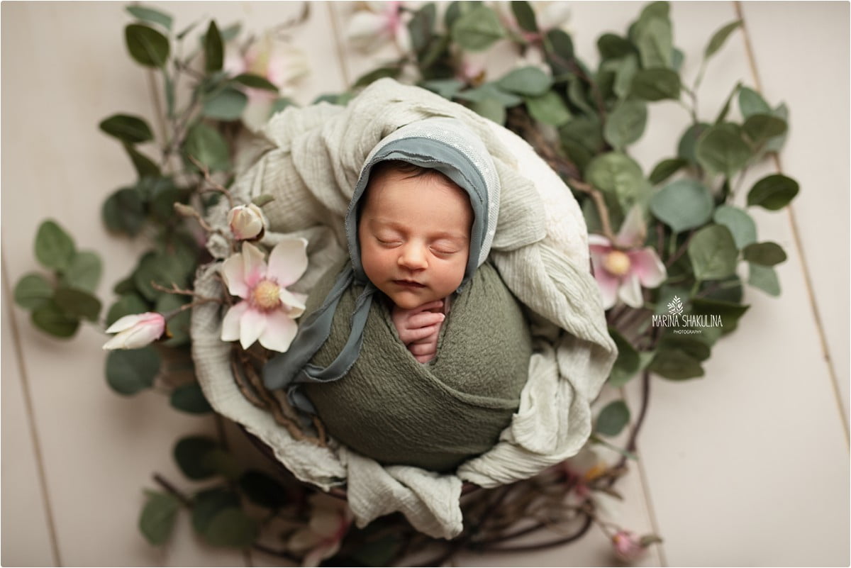 bimba fasciata in verde con cuffietta in cestino con fiori